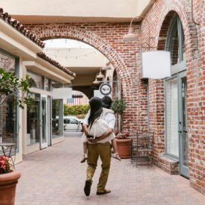 A father gives his daughter a piggyback ride through a charming brick alleyway, embodying family bonding.