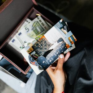 A hand holds nostalgic photos over a box filled with more images and keepsakes.