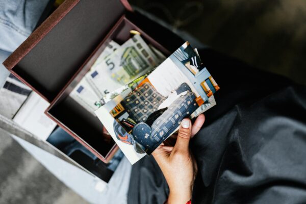 A hand holds nostalgic photos over a box filled with more images and keepsakes.