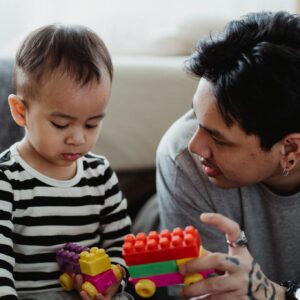 Father and son bonding at home playing with colorful building blocks.