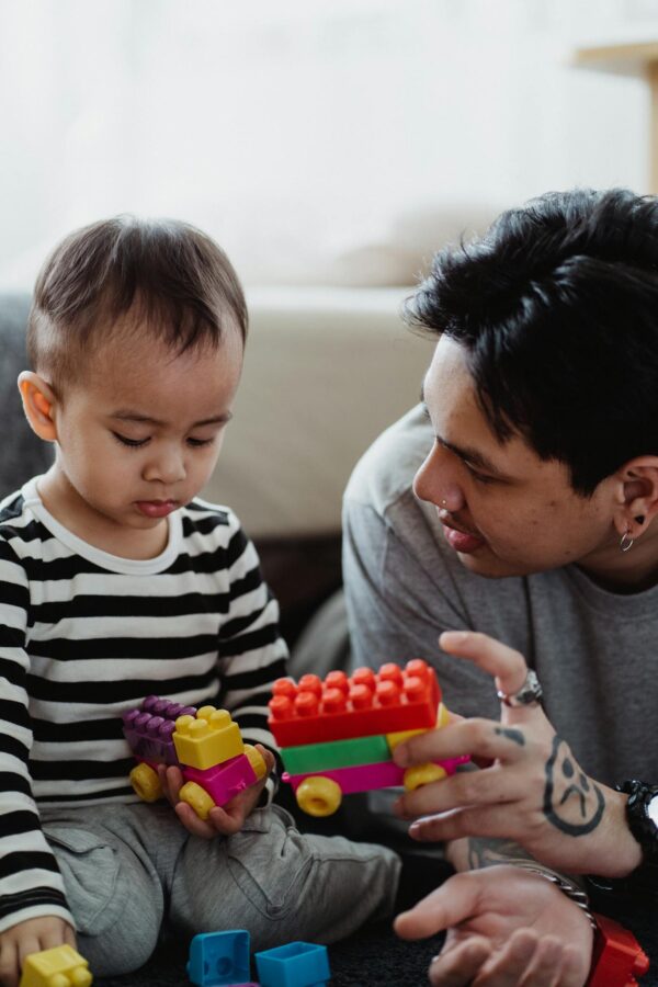 Father and son bonding at home playing with colorful building blocks.