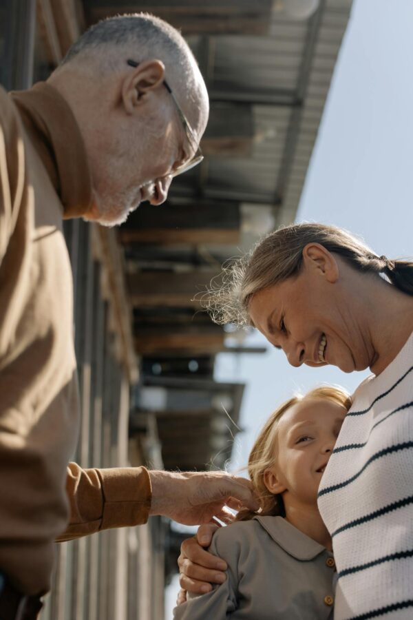 Heartwarming moment of grandparents sharing a joyful hug with their smiling granddaughter outdoors.