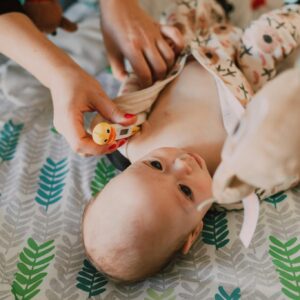 Parent using a thermometer for temperature check on a baby lying on a patterned bedspread.