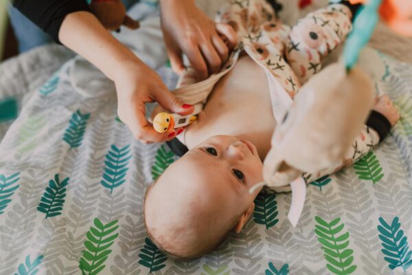 Parent using a thermometer for temperature check on a baby lying on a patterned bedspread.